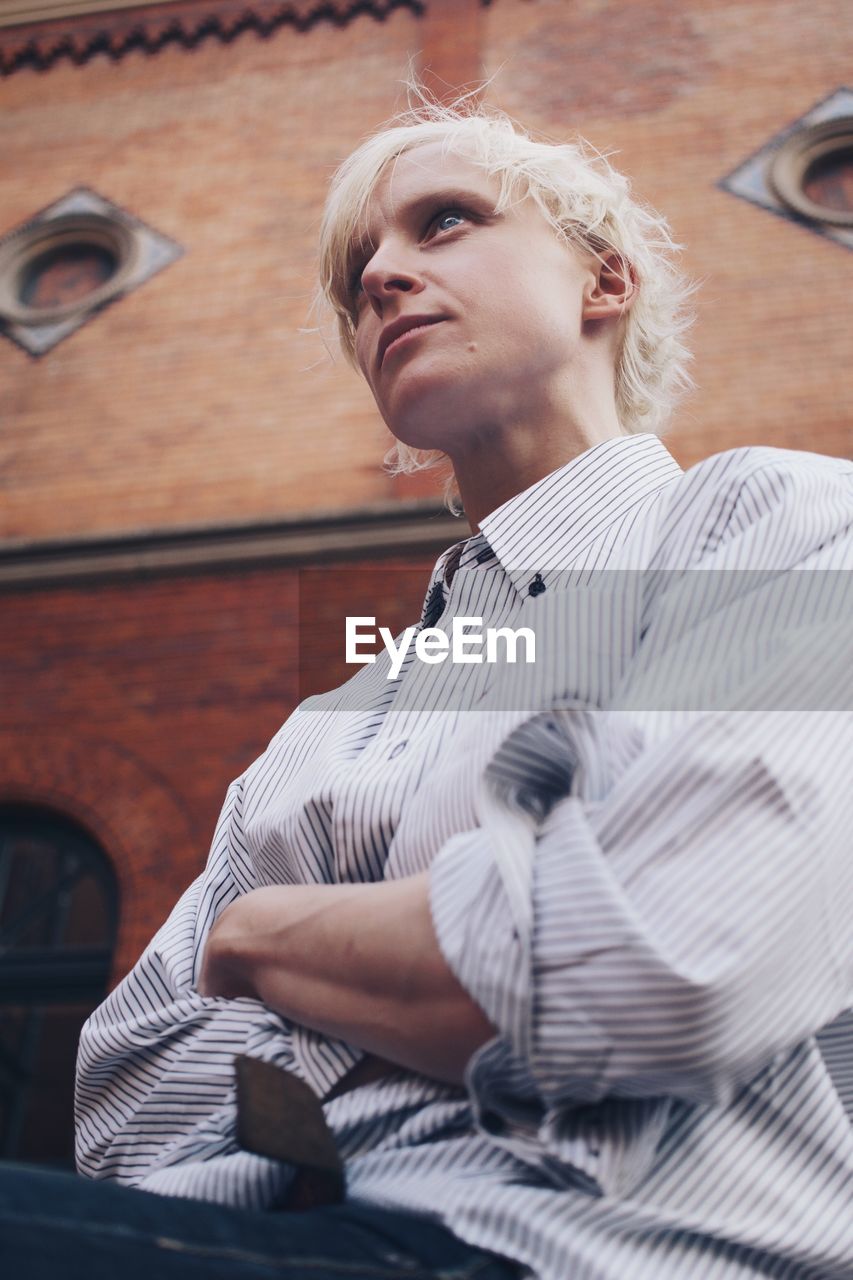 Low angle view of young woman looking away while sitting against wall