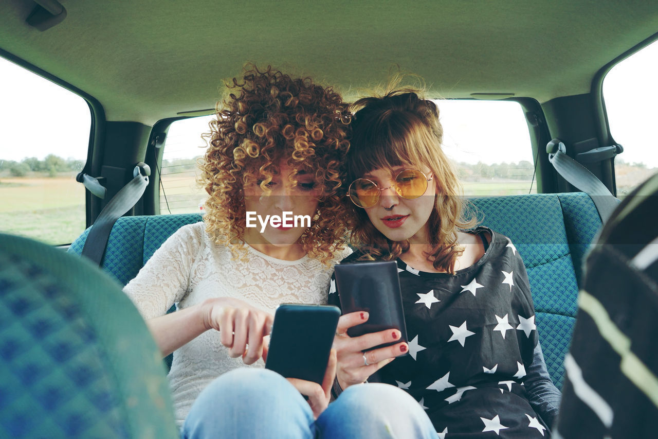 Friends using mobile phones while sitting in car