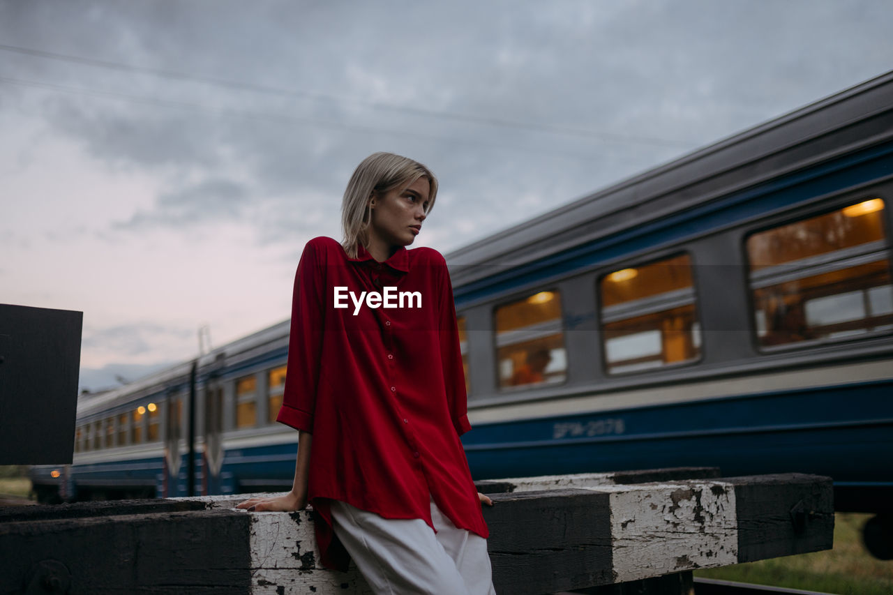 A blonde woman in a red shirt stands near a passing train