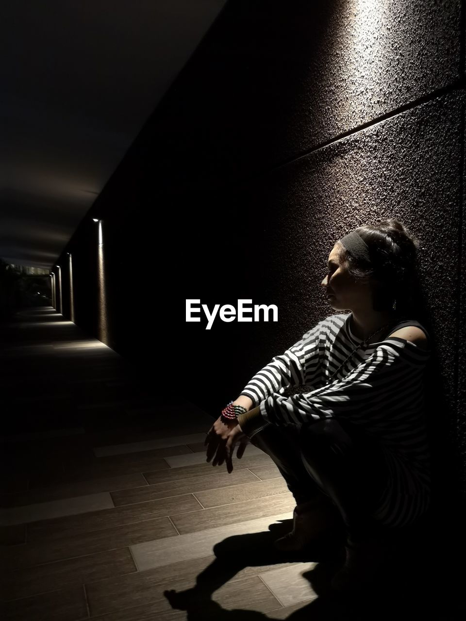 Side view of woman sitting on floor in dark corridor