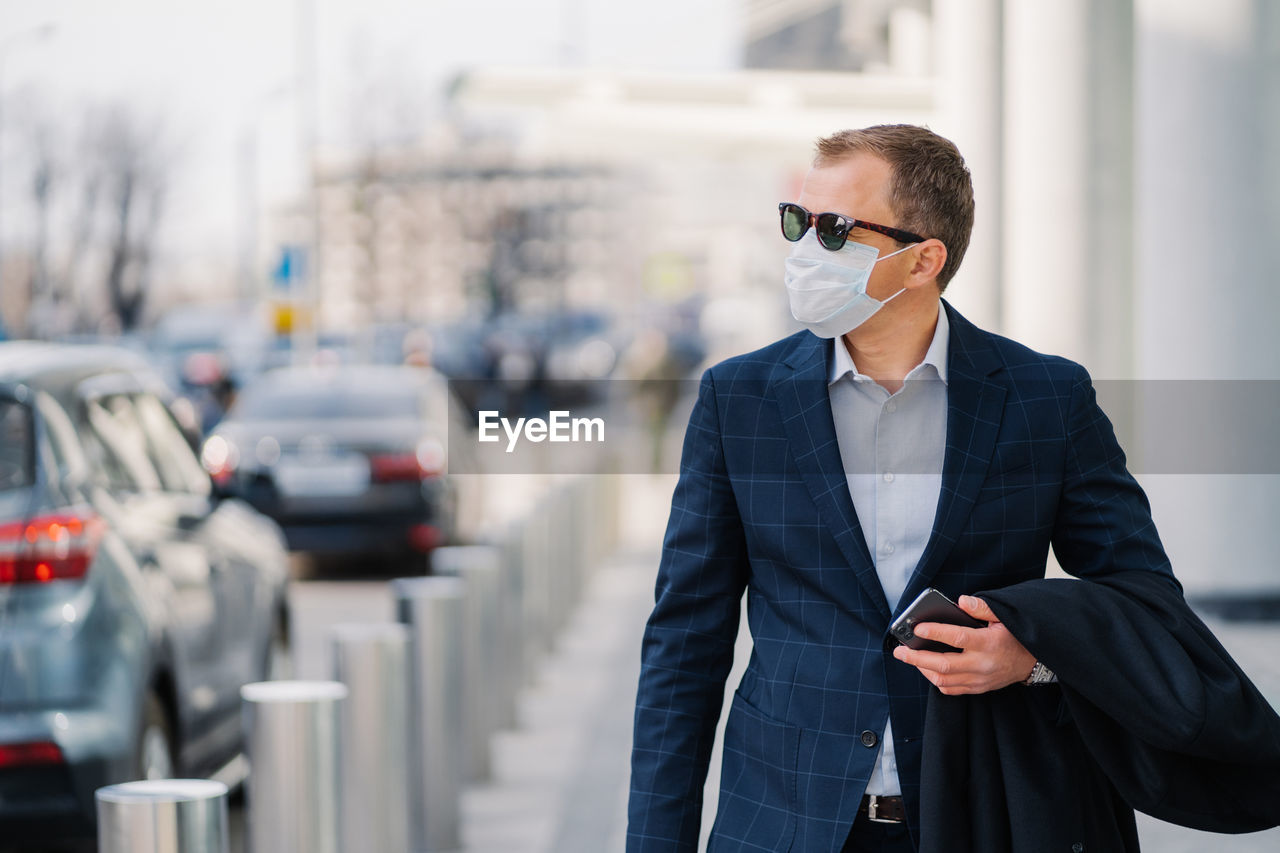 Businessman wearing mask walking on sidewalk in city