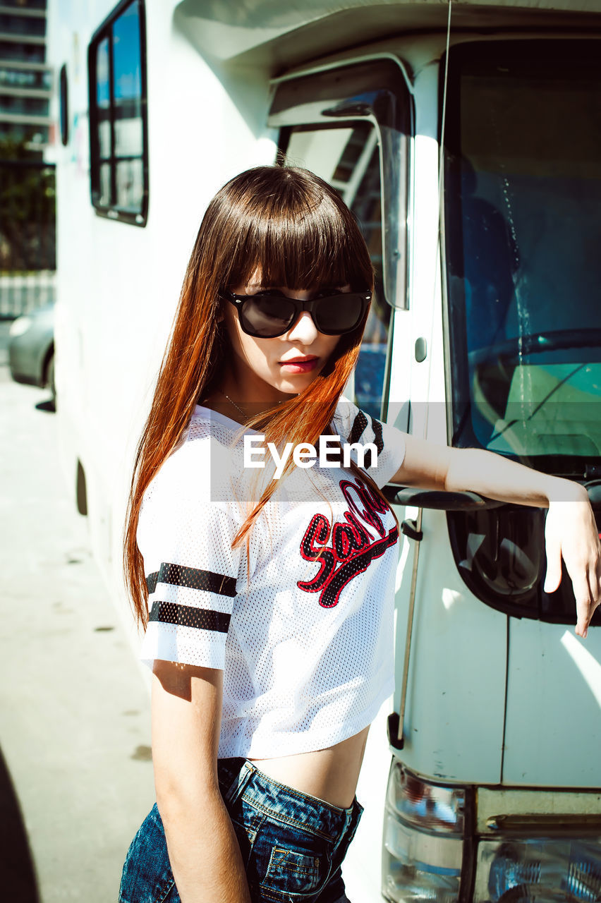 Portrait of beautiful young woman standing by truck during sunny day