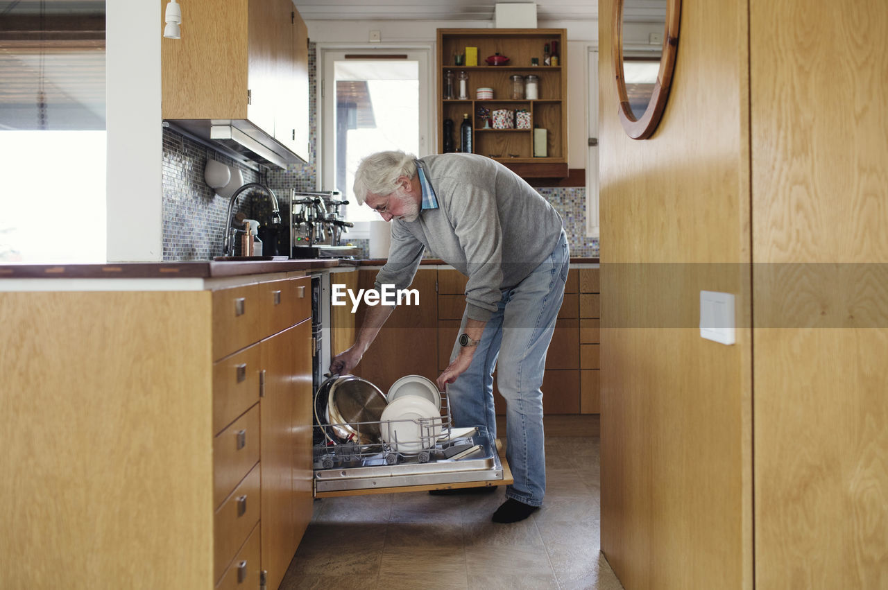 Senior man putting plates in dishwasher at kitchen