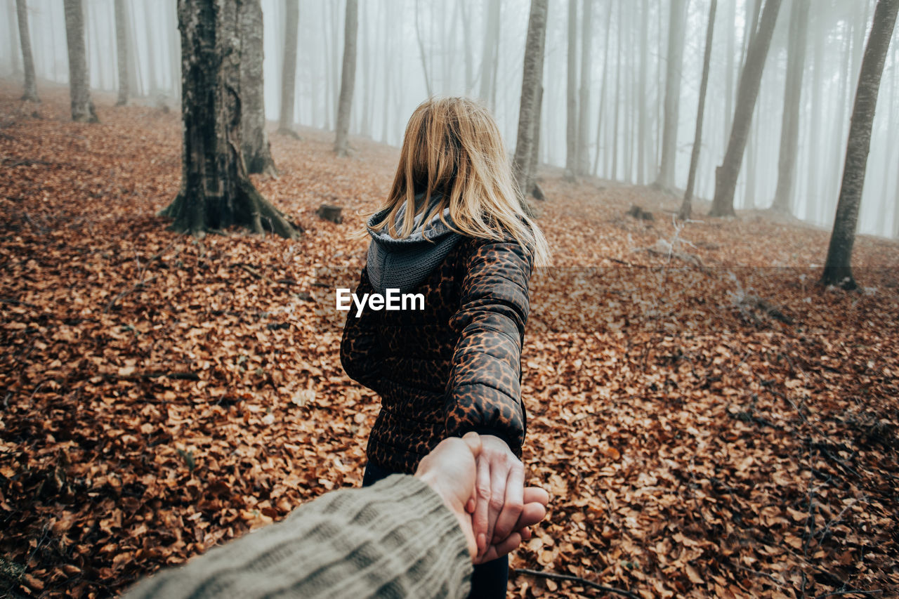 Cropped hand of man holding woman at forest during autumn