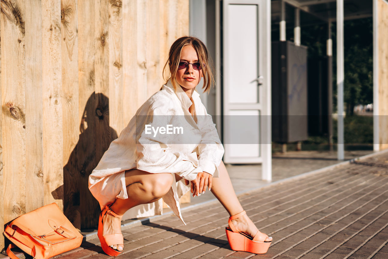 Full length of woman wearing sunglasses crouching on footpath