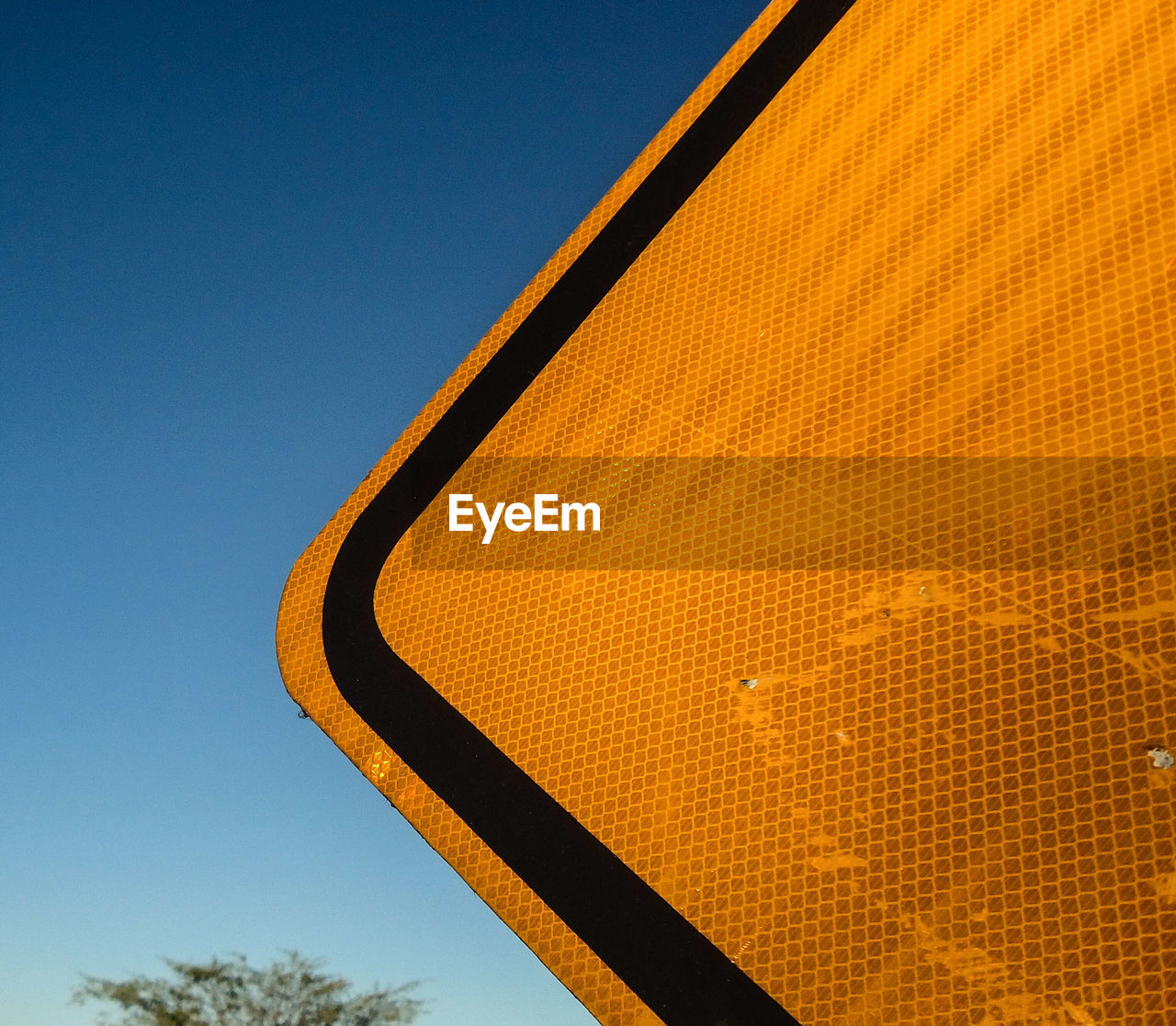 Partial view of a yellow traffic sign near a highway