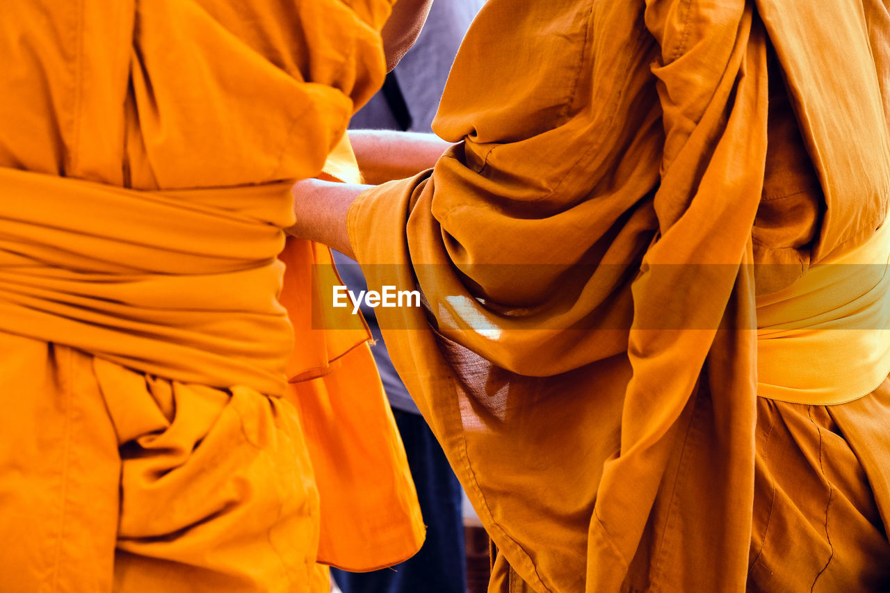 Midsection of monks wearing traditional clothing while standing outdoors