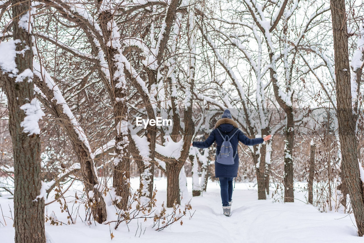 Rear view of woman wearing warm clothing with backpack walking on snow in forest