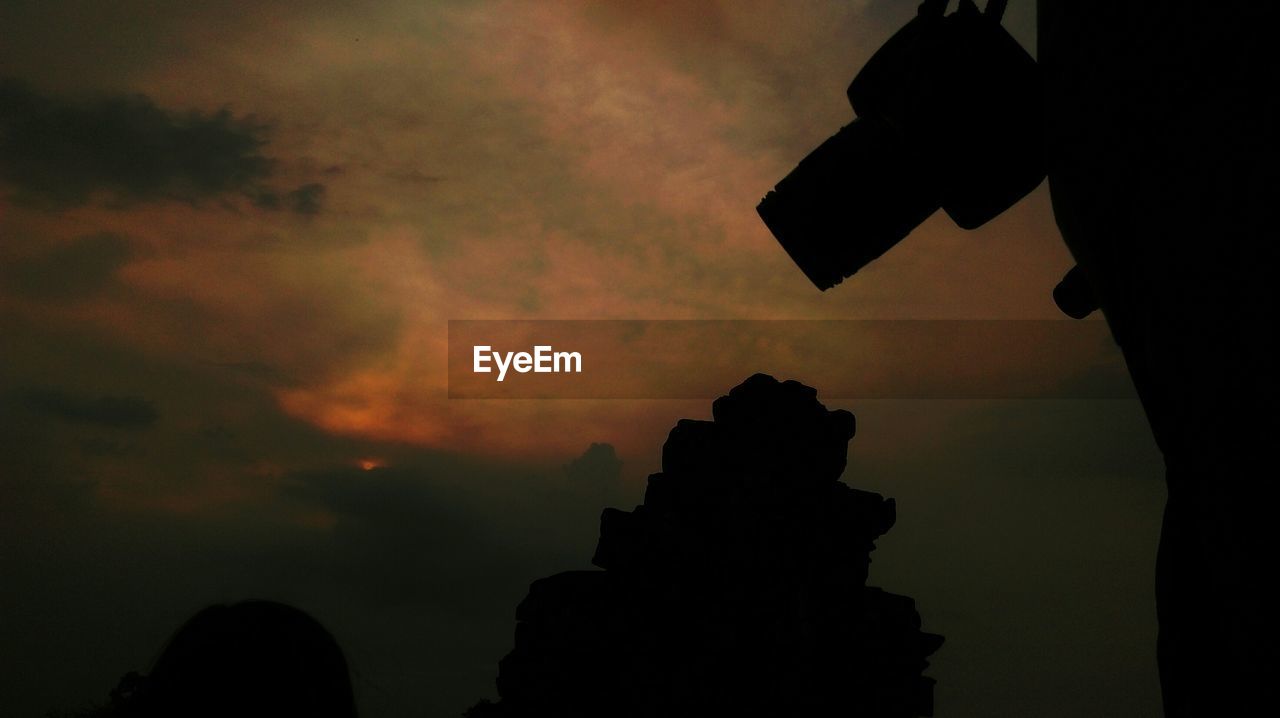 Cropped image of person with camera against cloudy sky at sunset