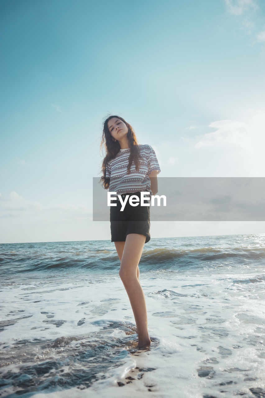 WOMAN STANDING ON BEACH AGAINST SKY