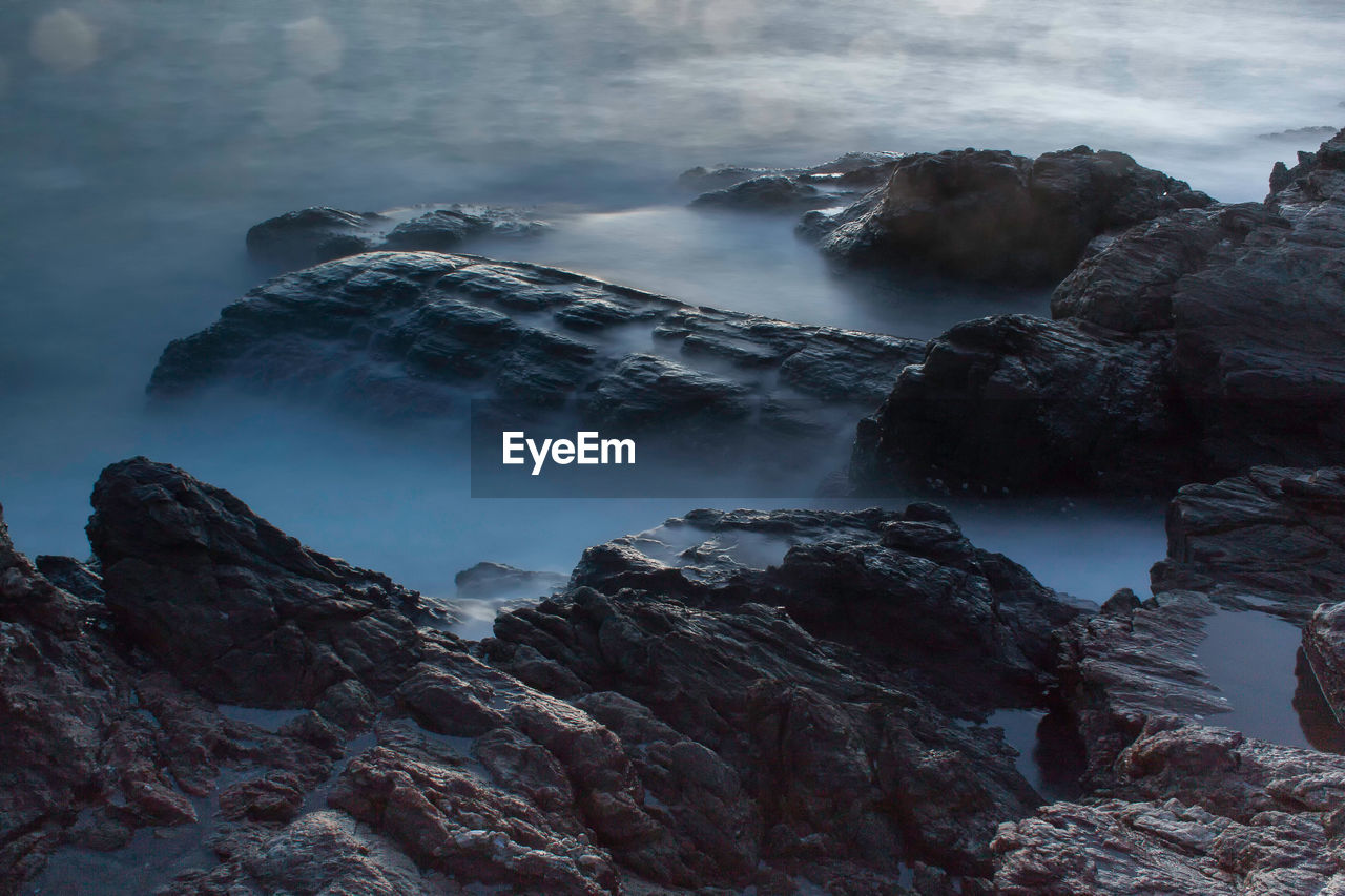 Scenic view of rock formation by sea against cloudy sky