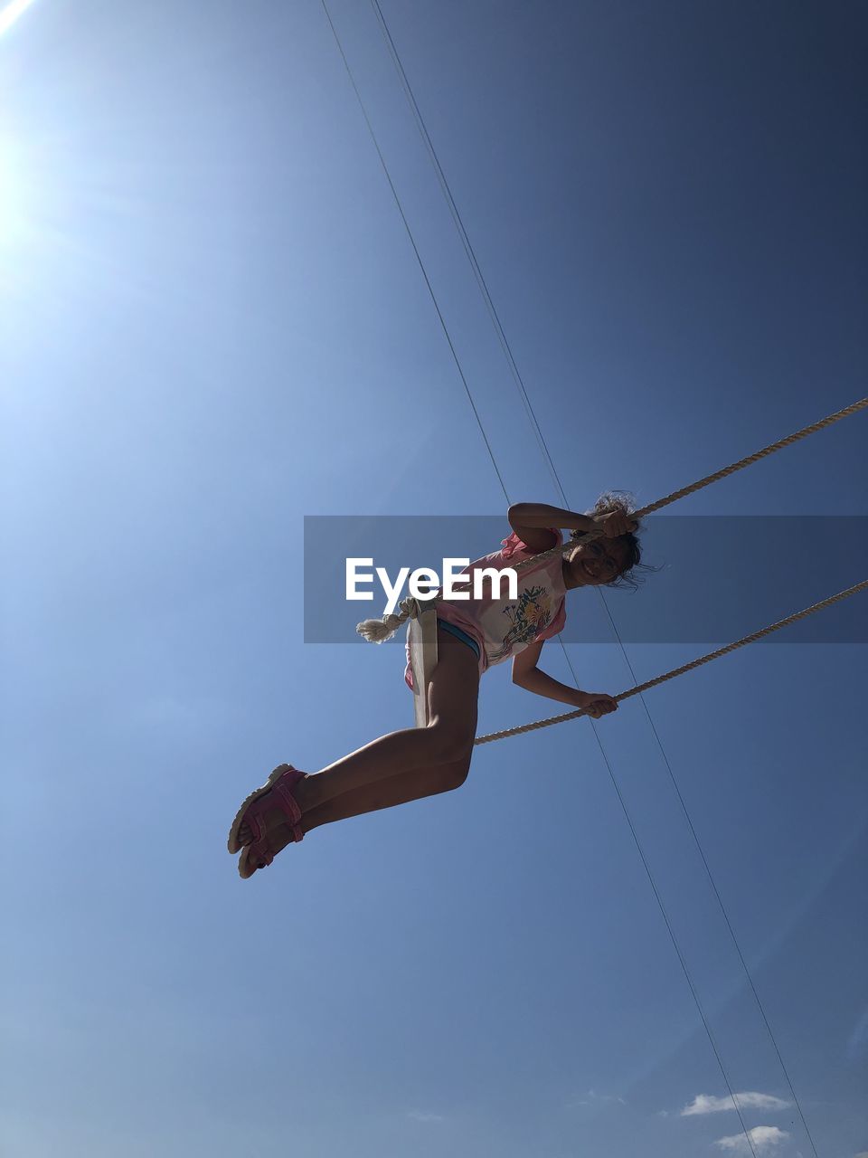 Low angle view of girl sitting on swing against blue sky