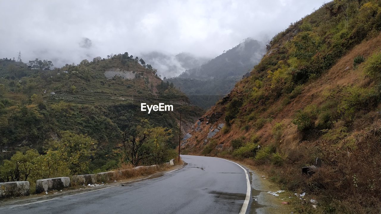 Road amidst trees and mountains against sky