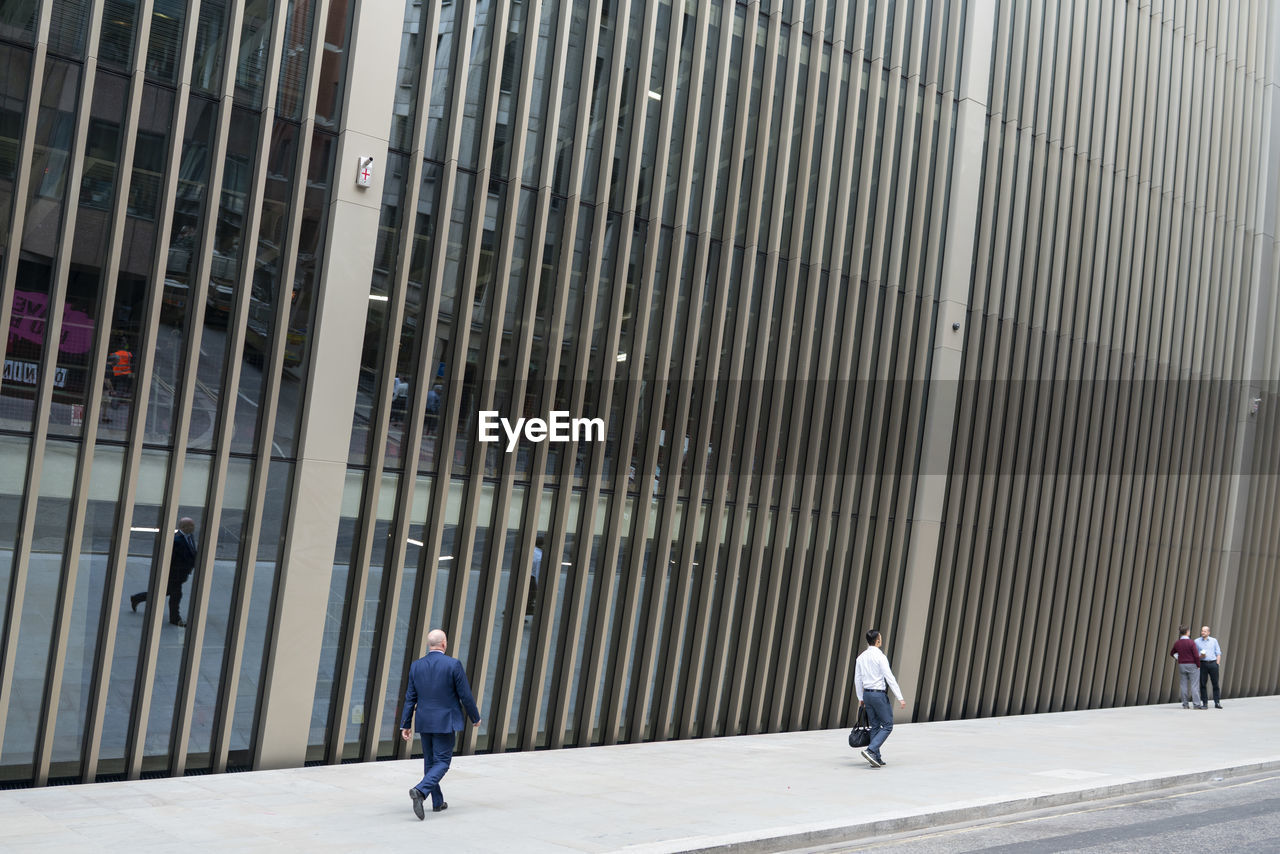 REAR VIEW OF PEOPLE WALKING ON SIDEWALK