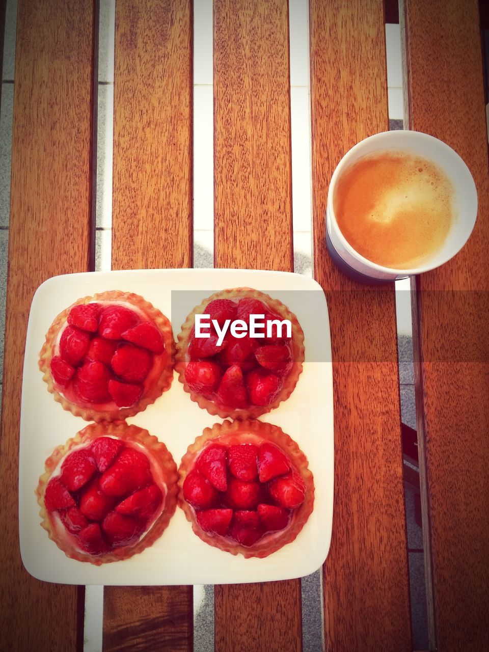 Directly above shot of strawberry tart served in plate by coffee on wooden table