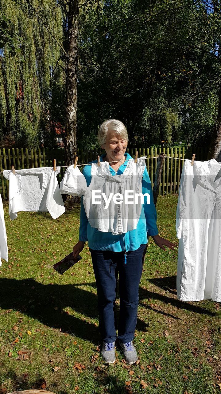 Full length of senior woman standing by clothesline in yard