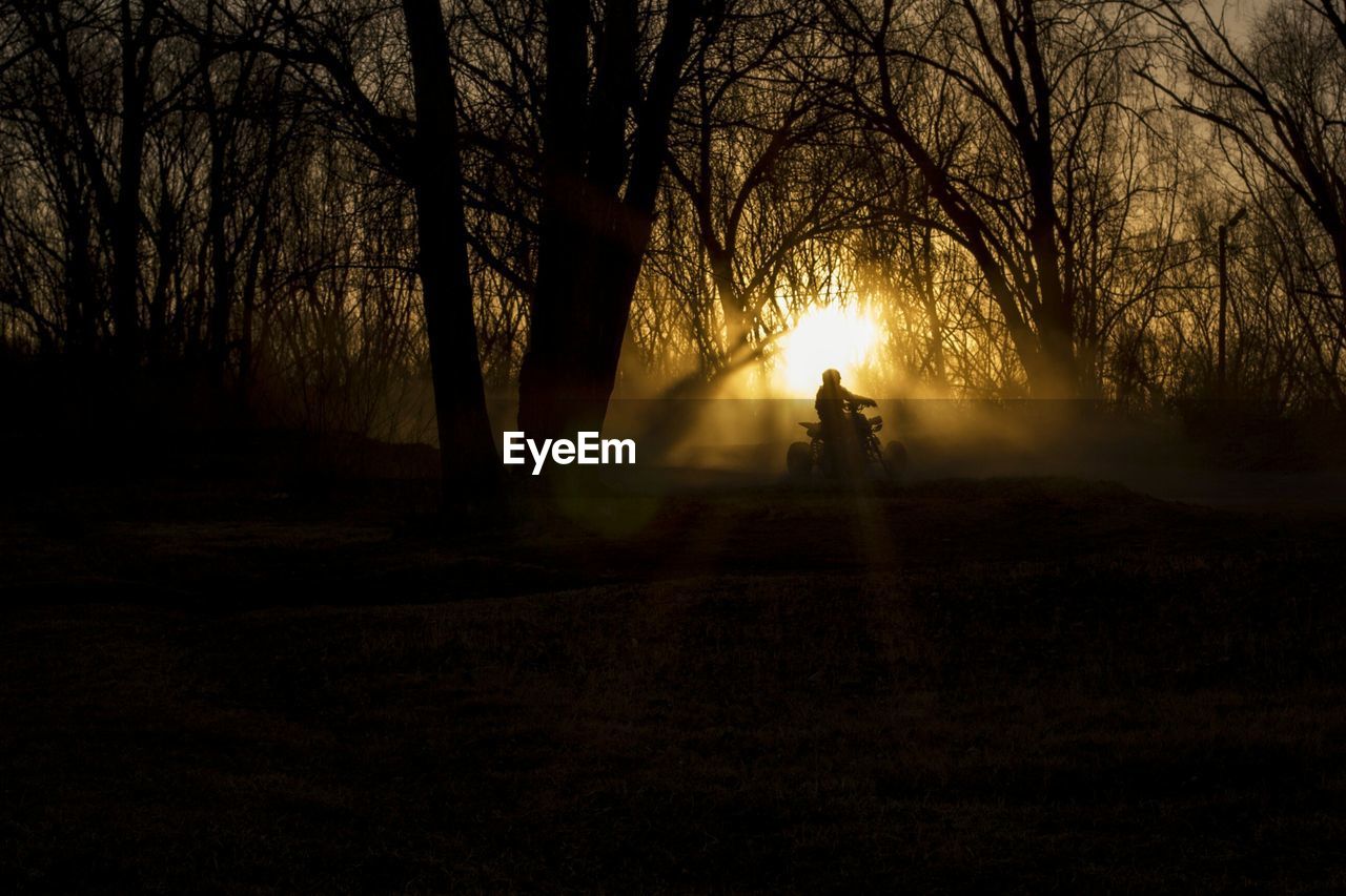 Silhouette person driving quadbike during sunset