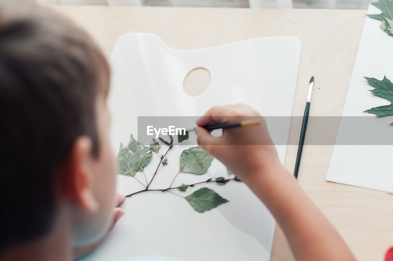 Close up of child sitting at desk and making picture from dry birch leaves. autumn activities 