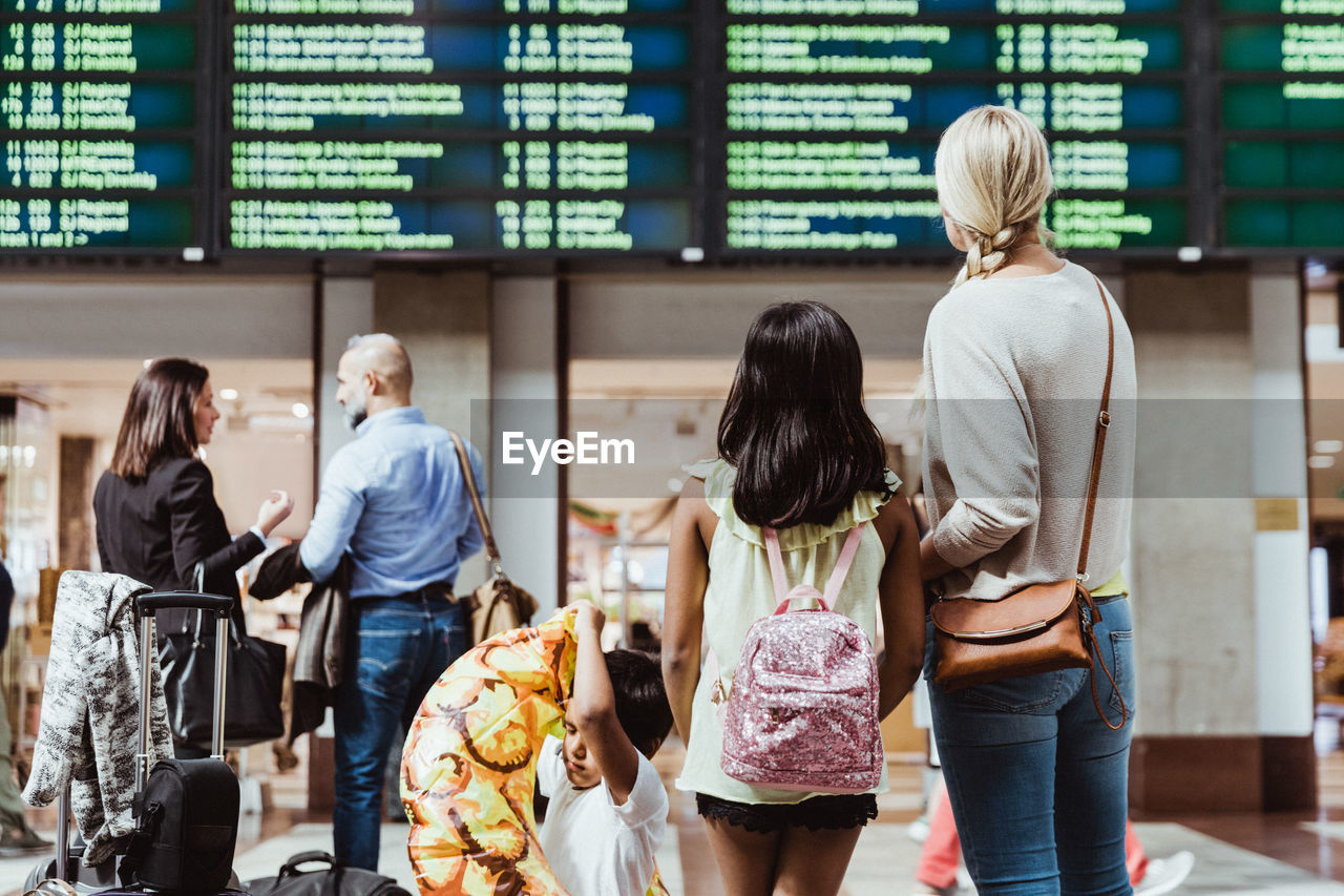 Family and business colleagues looking at arrival departure board while waiting in station