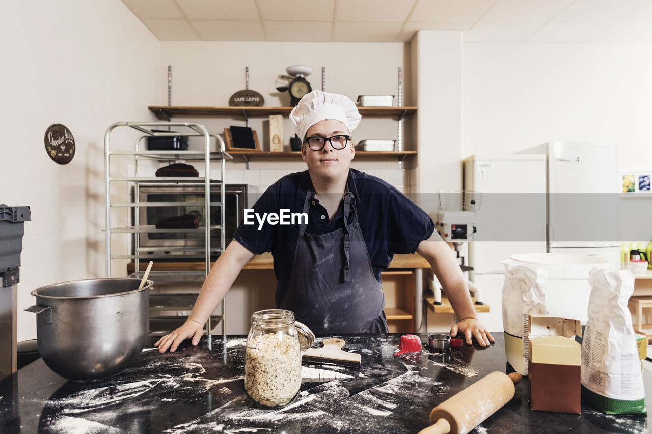 Portrait of confident young baker standing by kitchen counter