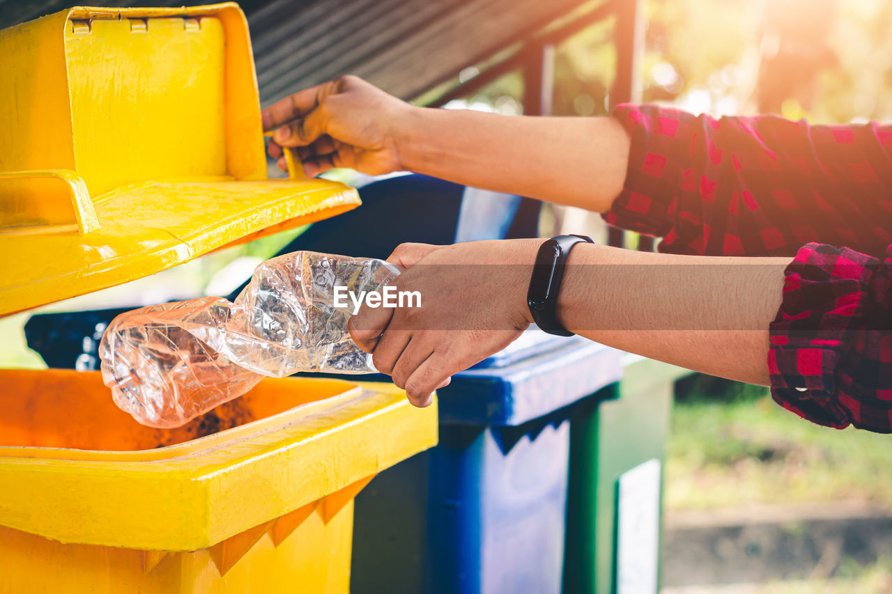 Midsection of man dumping plastic in garbage bin 