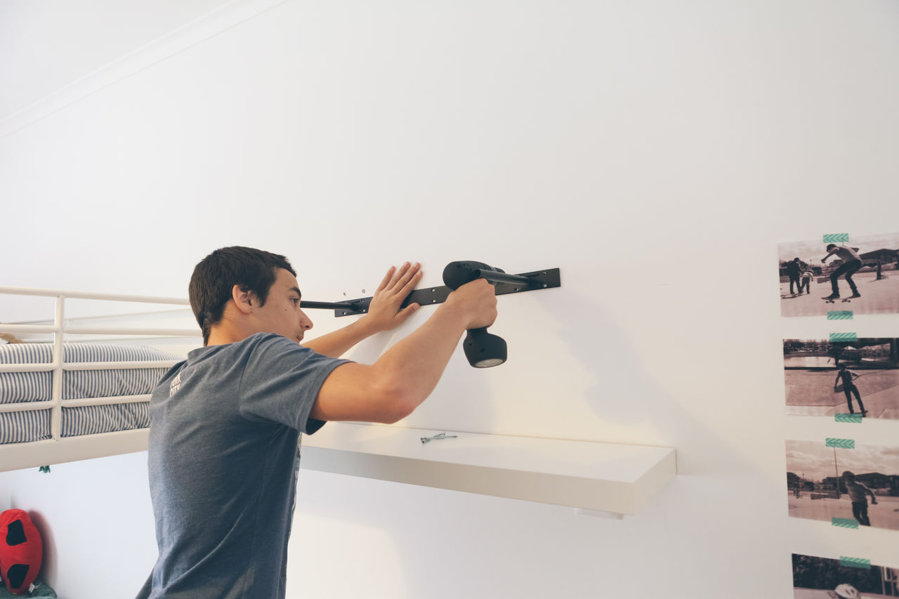 Rear view of man drilling rack on wall