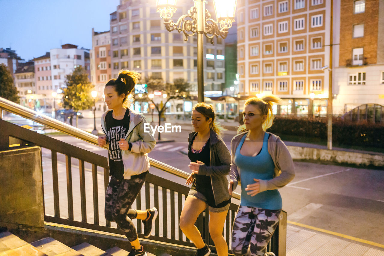 Women friends training running up stairs in city at night