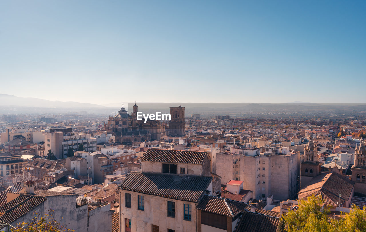 Drone view of residential buildings and trees located on streets of granada against cloudless blue sky in autumn in spain