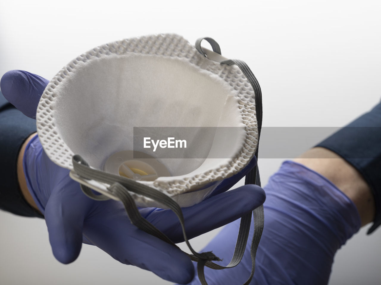 Close-up of person holding face mask against white background