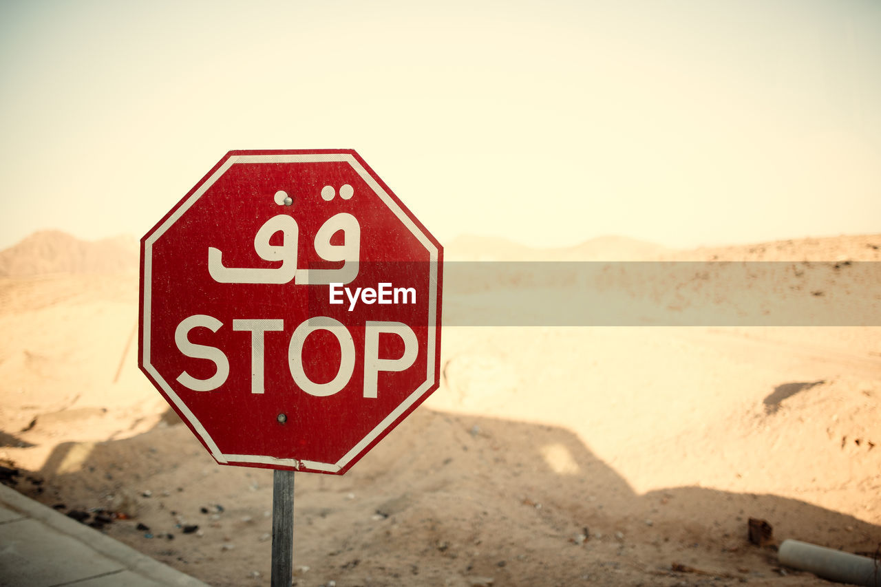 CLOSE-UP OF ROAD SIGN ON SAND AGAINST SKY