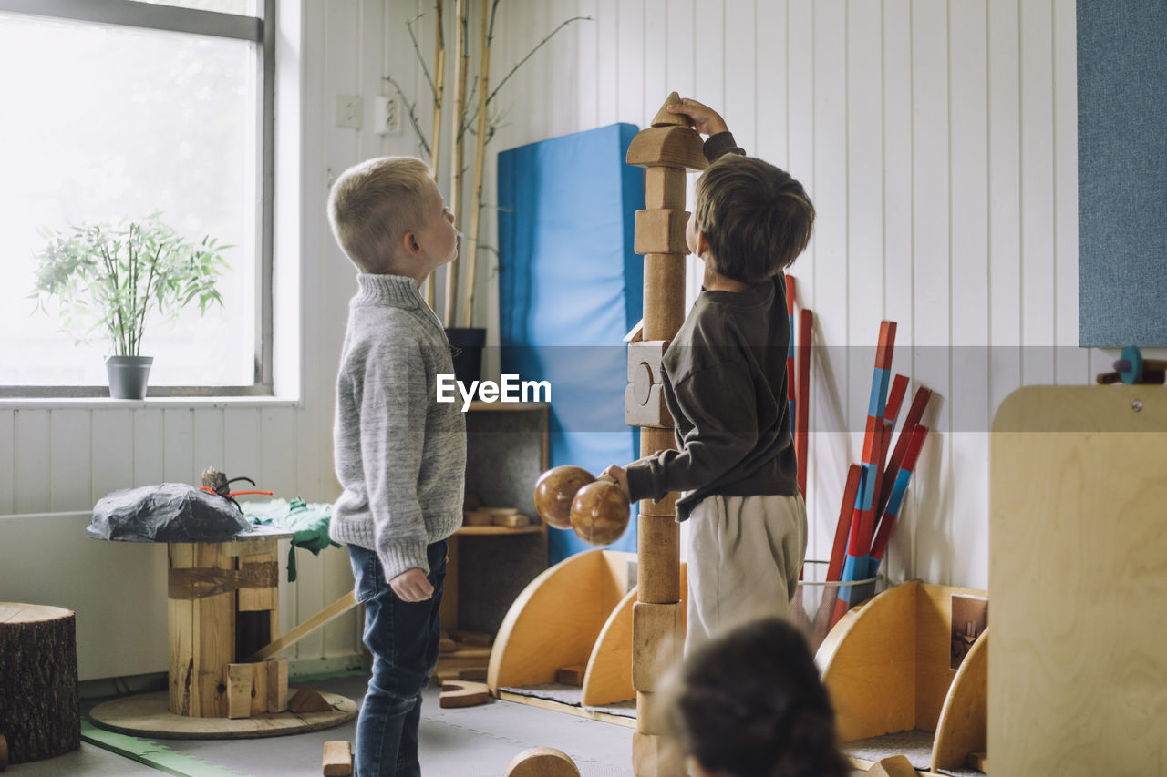 Boy stacking toy blocks while male friend looking at him in day care center