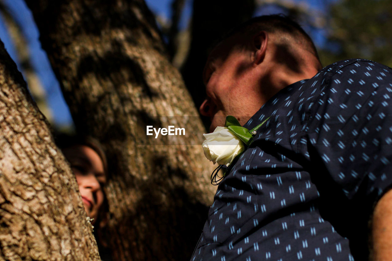 MAN STANDING BY TREE TRUNK