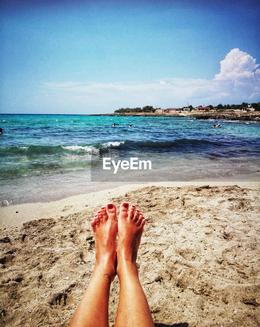 Low section of woman with feet up at beach against blue sky