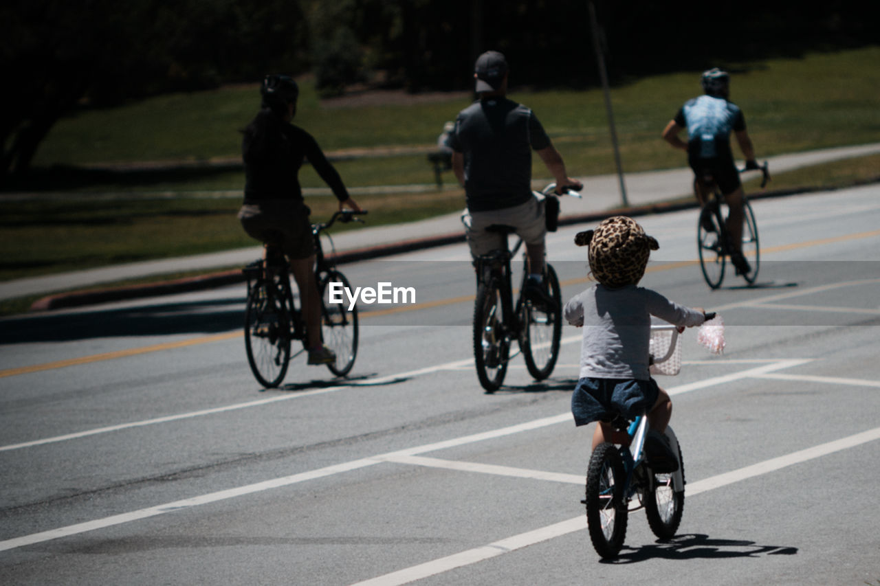Rear view of people bicycling on road