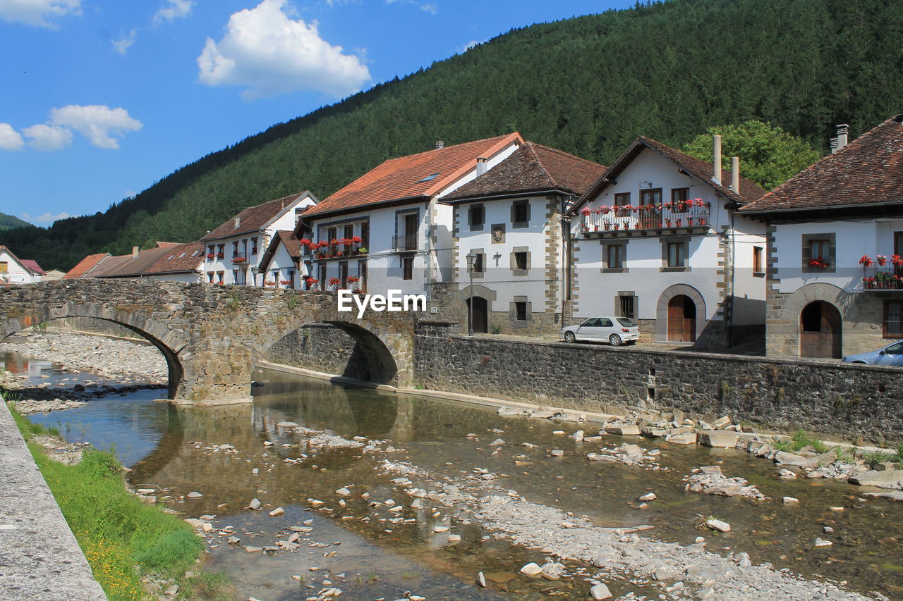 BRIDGE OVER RIVER BY BUILDINGS AGAINST SKY