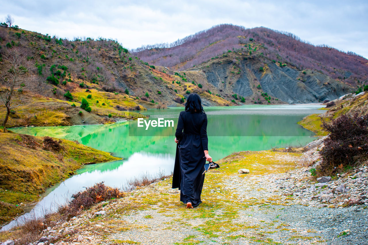 Rear view of woman walking by lake against mountain