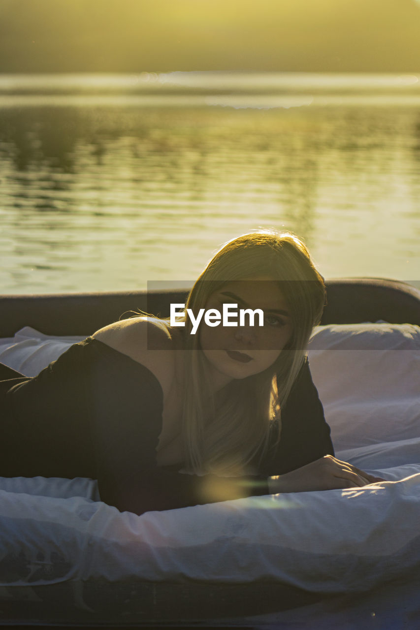 Young woman lies on a mattress on the background of water, where the sunset is reflected on water