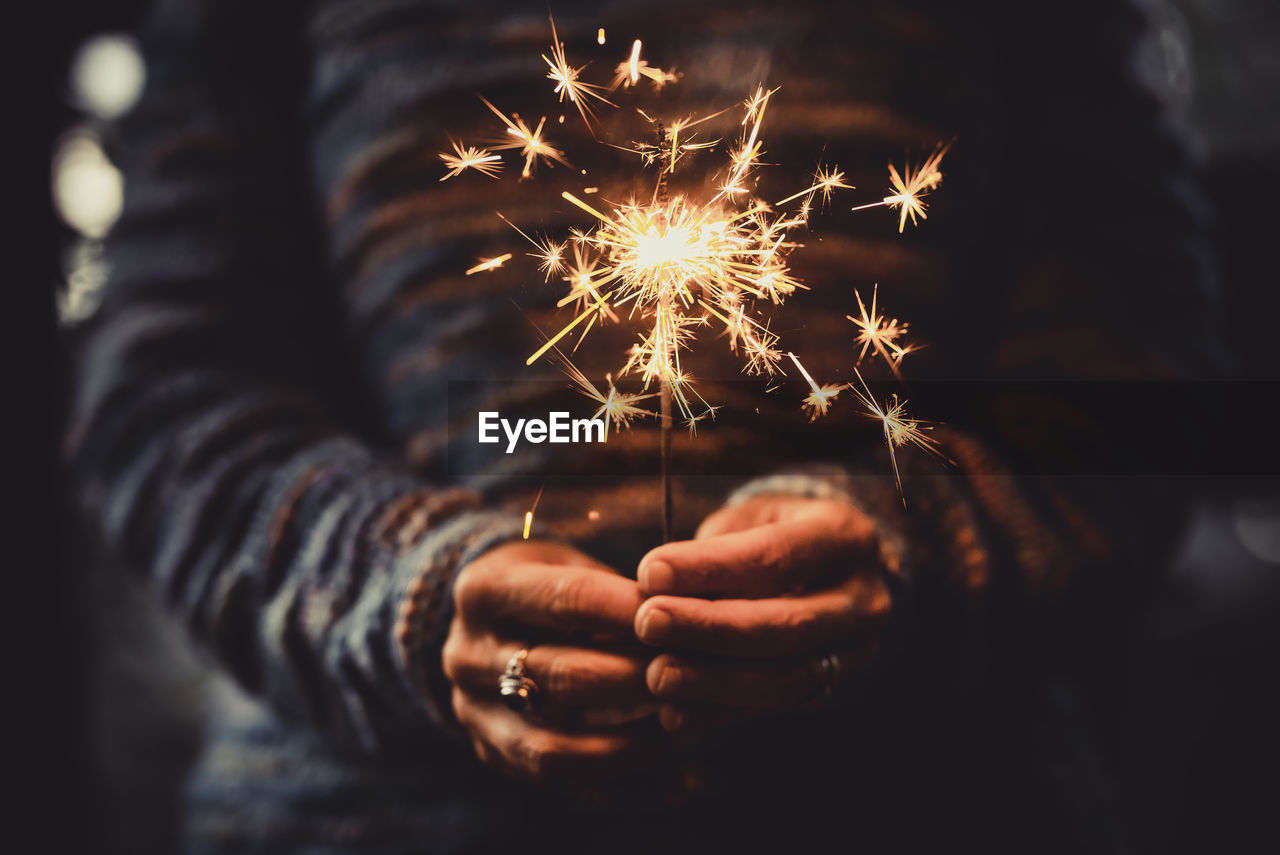 Midsection of woman holding sparkler at night