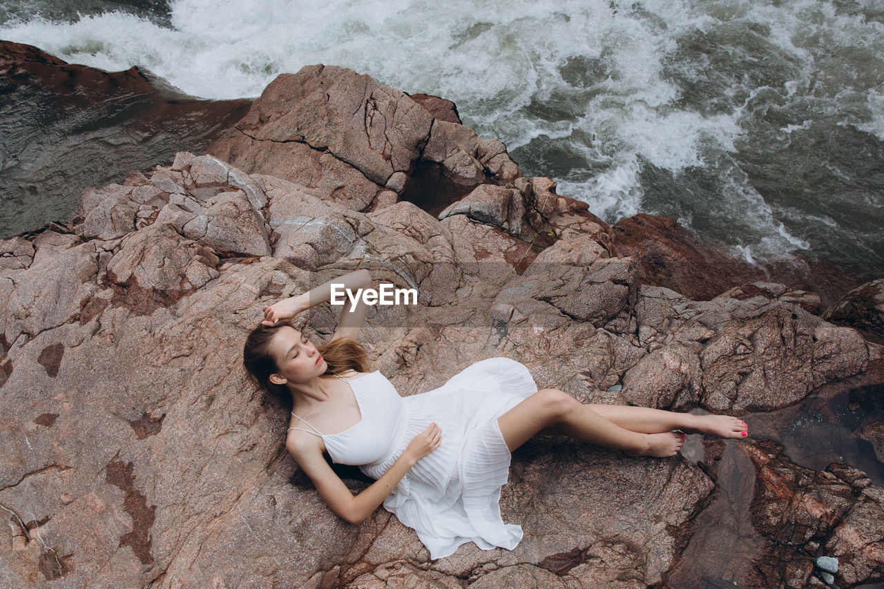 High angle view of woman relaxing on cliff by sea