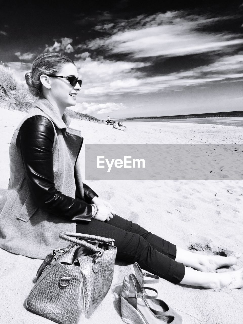 Woman wearing sunglasses sitting on sand at beach against sky