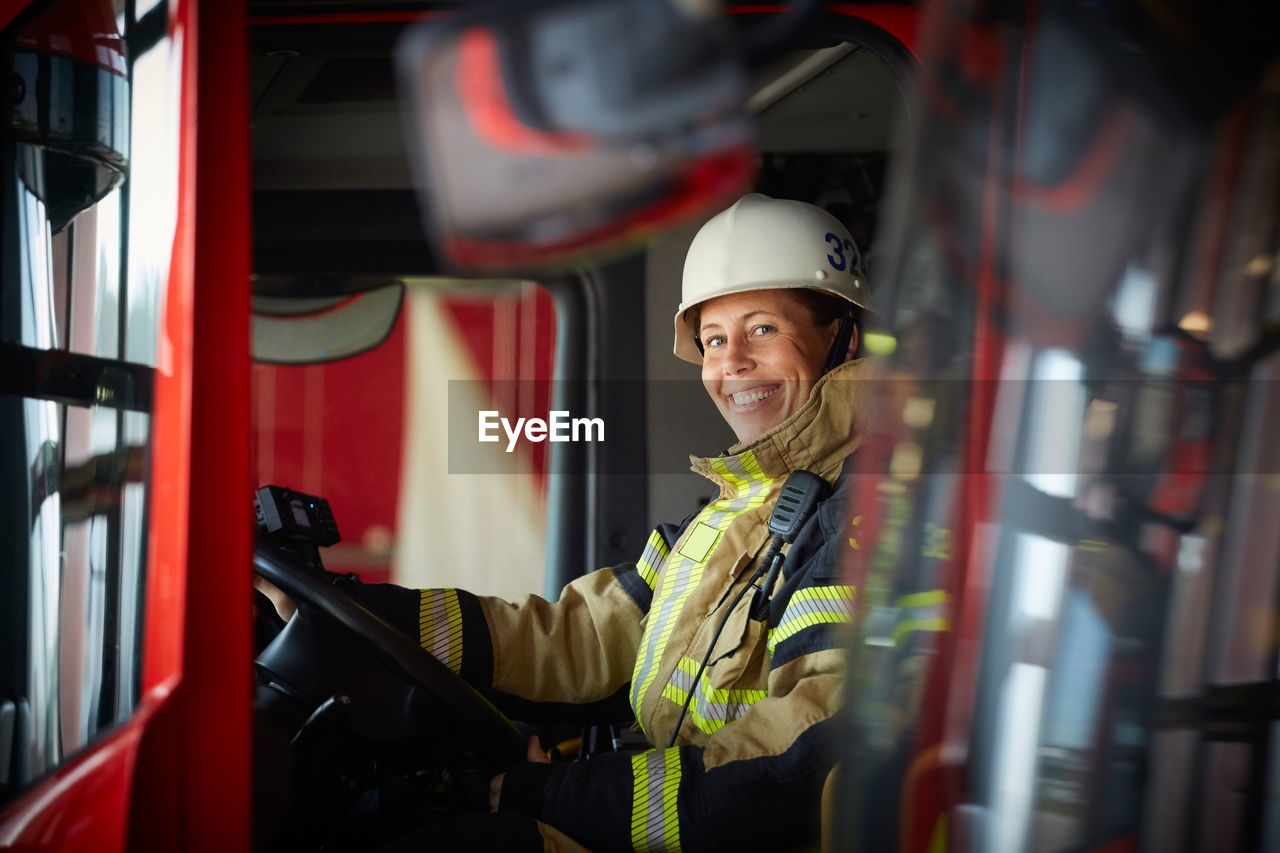 Portrait of smiling female firefighter sitting in fire truck at fire station