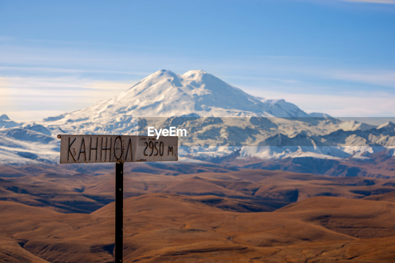 Information sign on snowcapped mountains against sky