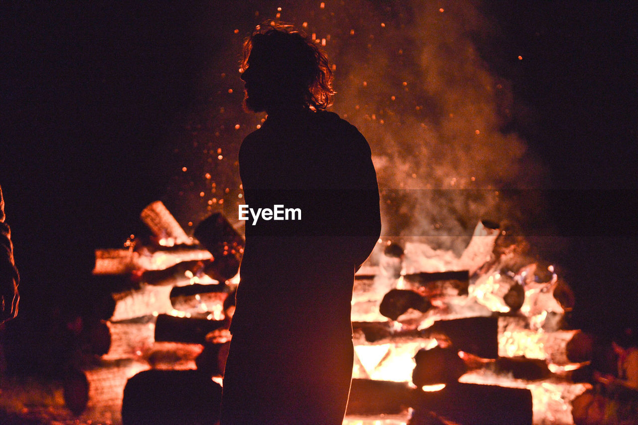 Silhouette man standing against bonfire at night