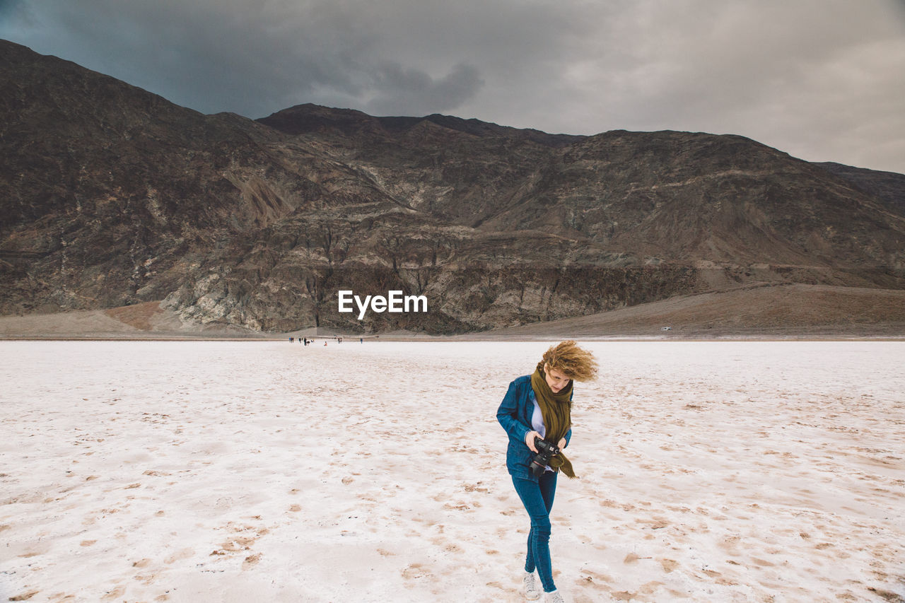 Young woman holding camera walking at death valley national park against sky