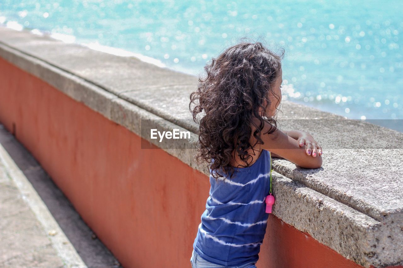 Side view of girl looking at sea while standing by retaining wall