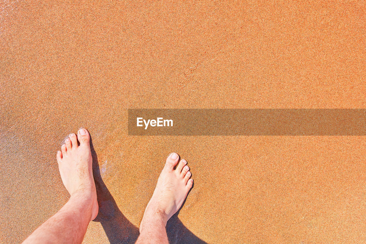 LOW SECTION OF MAN STANDING ON BEACH