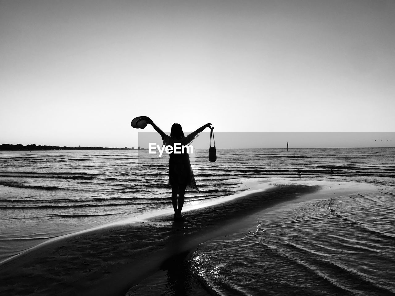 Silhouette woman holding bag and hat standing in beach against sky