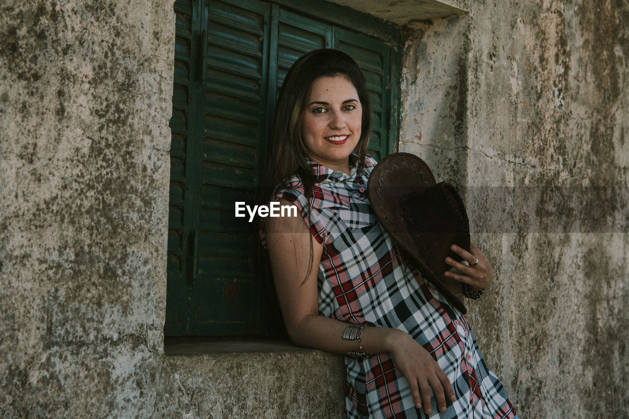 Portrait of woman standing by window of built structure