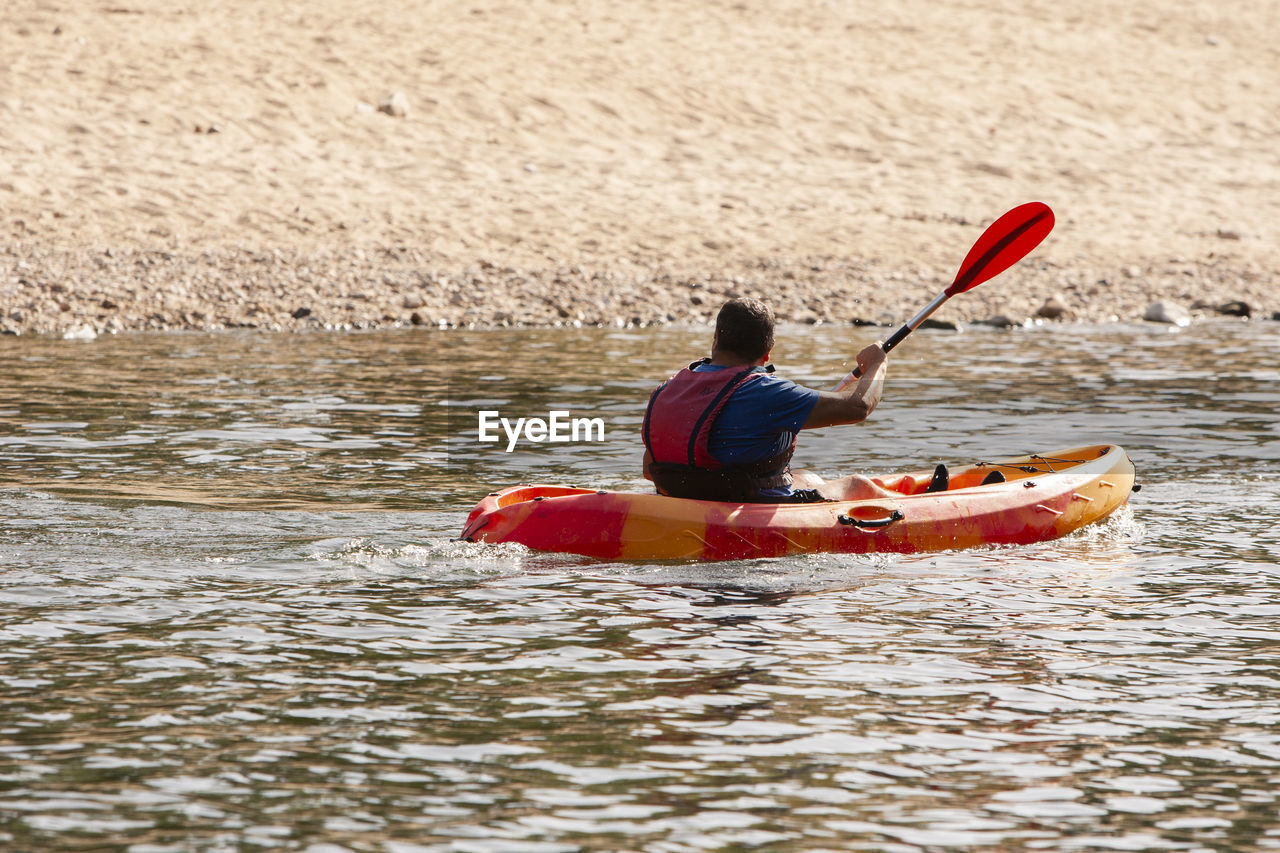 water, boat, kayak, oar, kayaking, nautical vessel, canoeing, transportation, leisure activity, adventure, vehicle, nature, sports, sea kayak, men, adult, sports equipment, one person, watercraft, lifestyles, life jacket, boating, canoe, rear view, recreation, motion, paddle, holiday, vacation, trip, day, river, outdoors, water sports, sitting, travel, mode of transportation, activity, weekend activities, outdoor pursuit, waist up, exercising, summer, paddling, boats and boating--equipment and supplies, beauty in nature, relaxation, red, beach