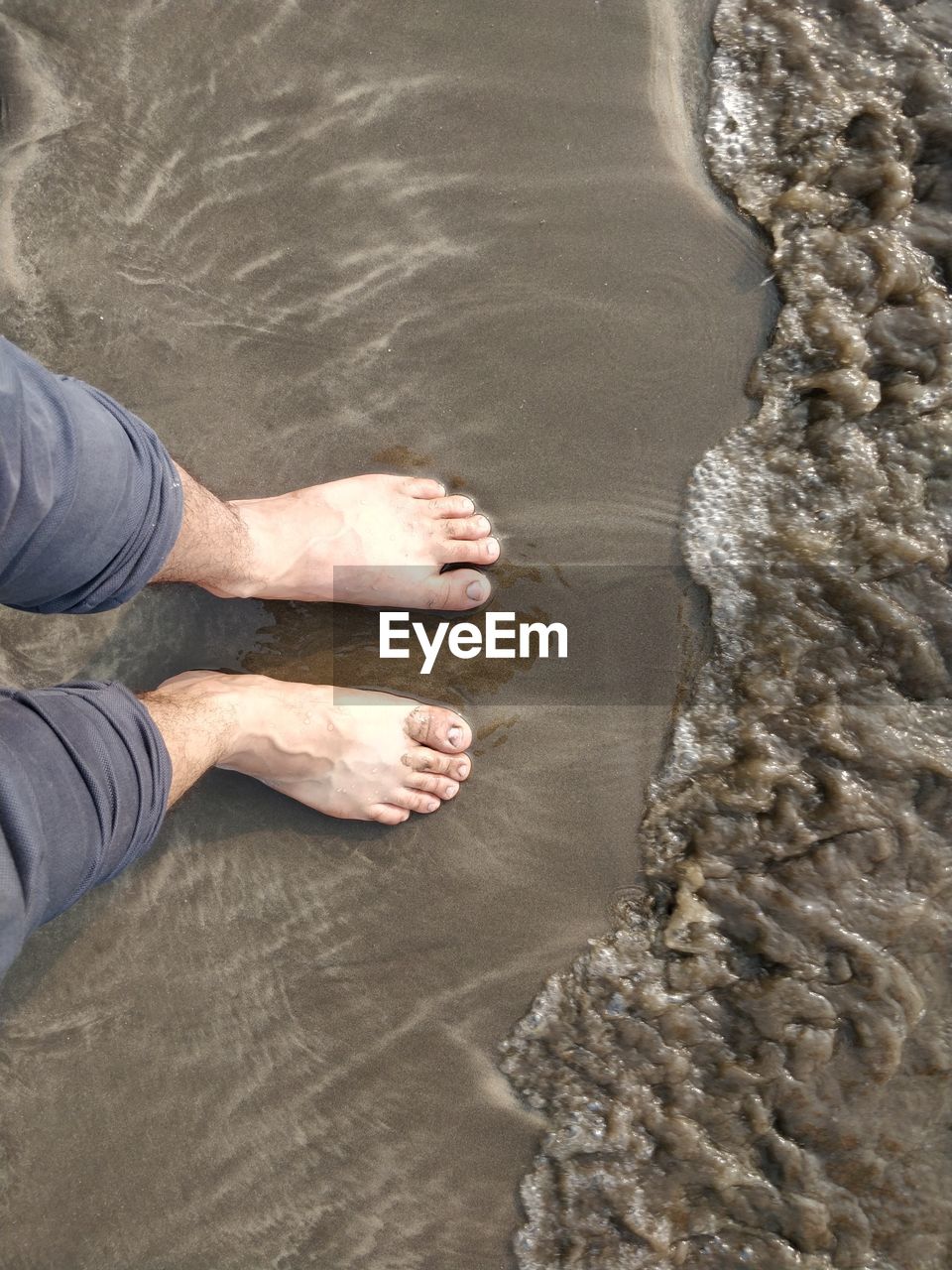 LOW SECTION OF MAN STANDING IN SEA WATER